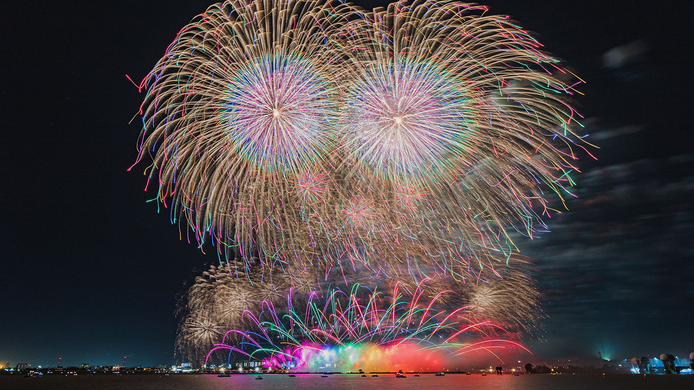 三重県桑名の花火。上空には二つの大玉の花火が上がり、海面には鮮やかな虹色の花火が。